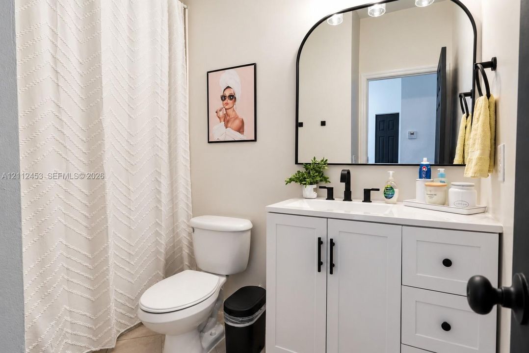 White vanity with quartz countertop, arch-top mirror with matte black frame, matte black widespread faucet, and matching cabinet hardware