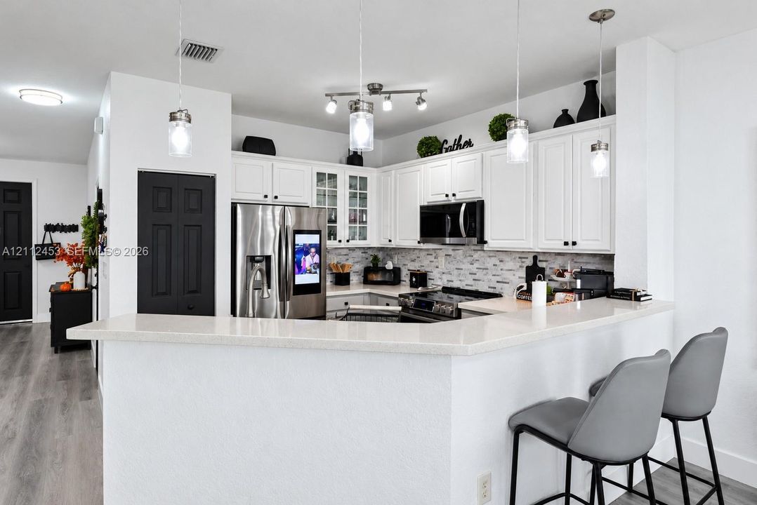 Kitchen featuring white cabinetry, solid surface countertops, a mosaic tile backsplash, stainless steel appliances, and pendant lighting