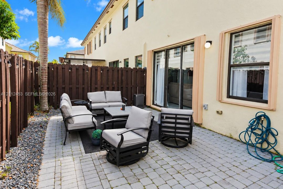 Private rear patio featuring stone-paver hardscaping, enclosed by a wood-slat privacy fence, with sliding glass door entry