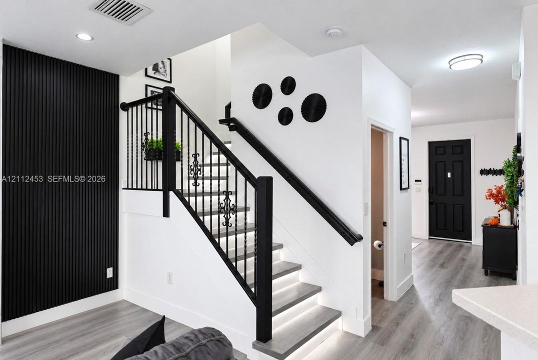 Staircase featuring black vertical slatted wall paneling, iron railings with decorative filigree, integrated riser lighting, and wood-finish flooring throughout