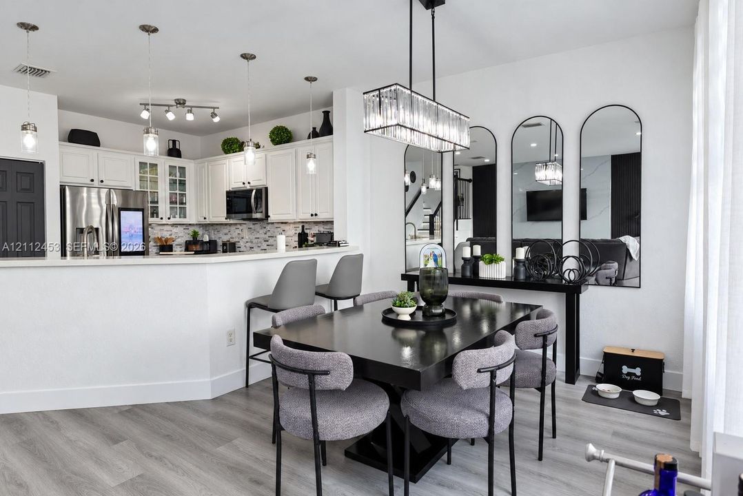 Kitchen featuring white cabinetry, a neutral tiled backsplash, and a breakfast bar, complemented by wood-finish flooring and a contemporary rectangular crystal chandelier