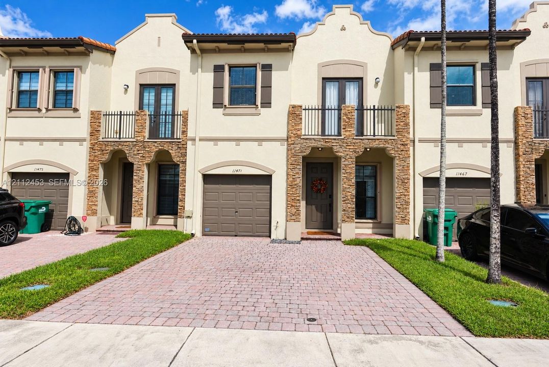 Multi-story stucco exterior featuring stacked stone accents, second-story balconies with wrought-iron railings, paved driveway, and attached garages