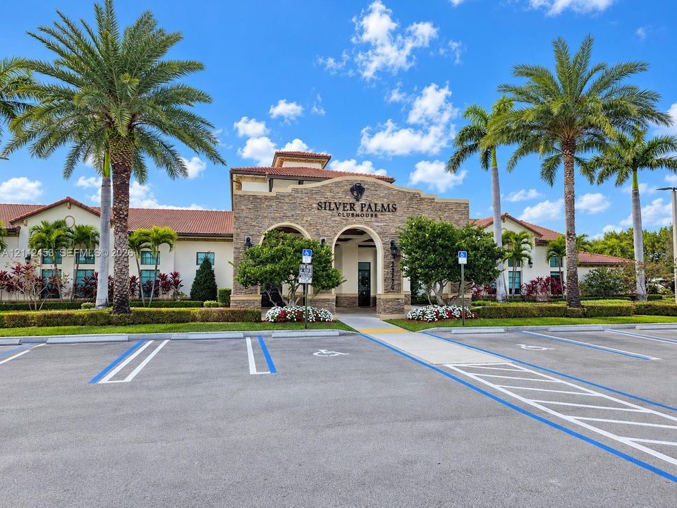 Silver Palms clubhouse exterior featuring stacked stone masonry, arched entryway, clay tile roof, and mature palm tree landscaping