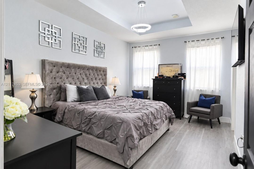 Tray ceiling featuring a modern circular pendant light, neutral wall paint, and wood-finish flooring
