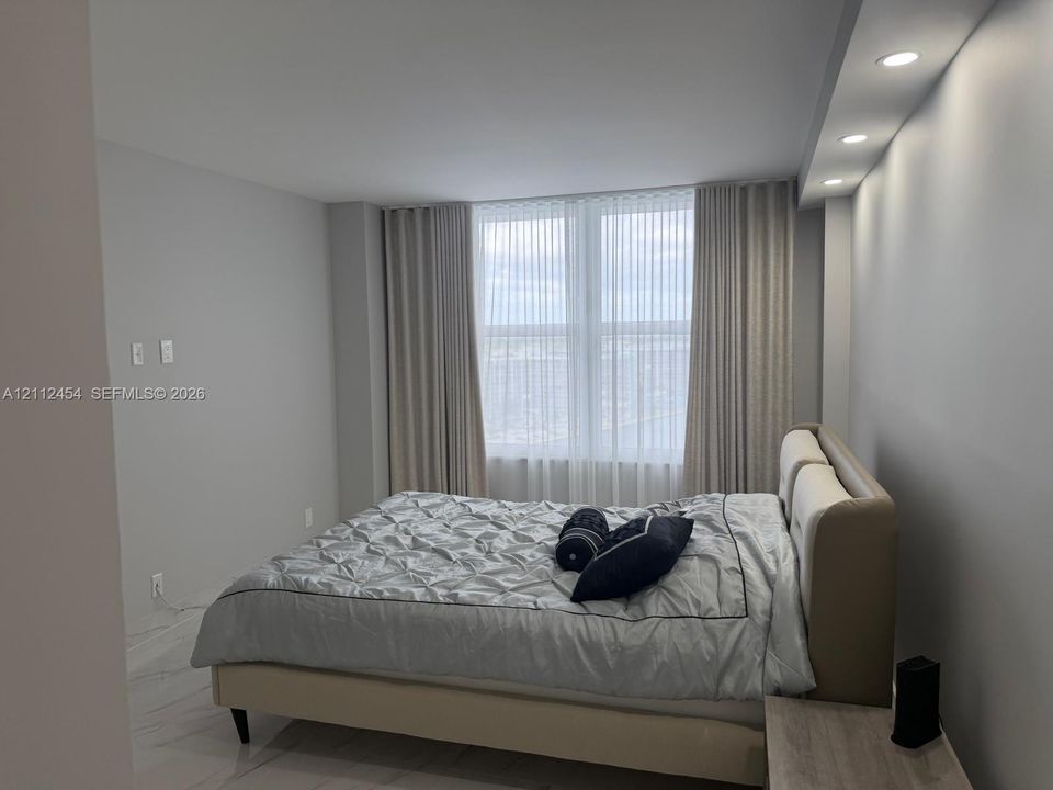 Large windows with floor-to-ceiling drapery, recessed soffit lighting, and high-gloss tile flooring