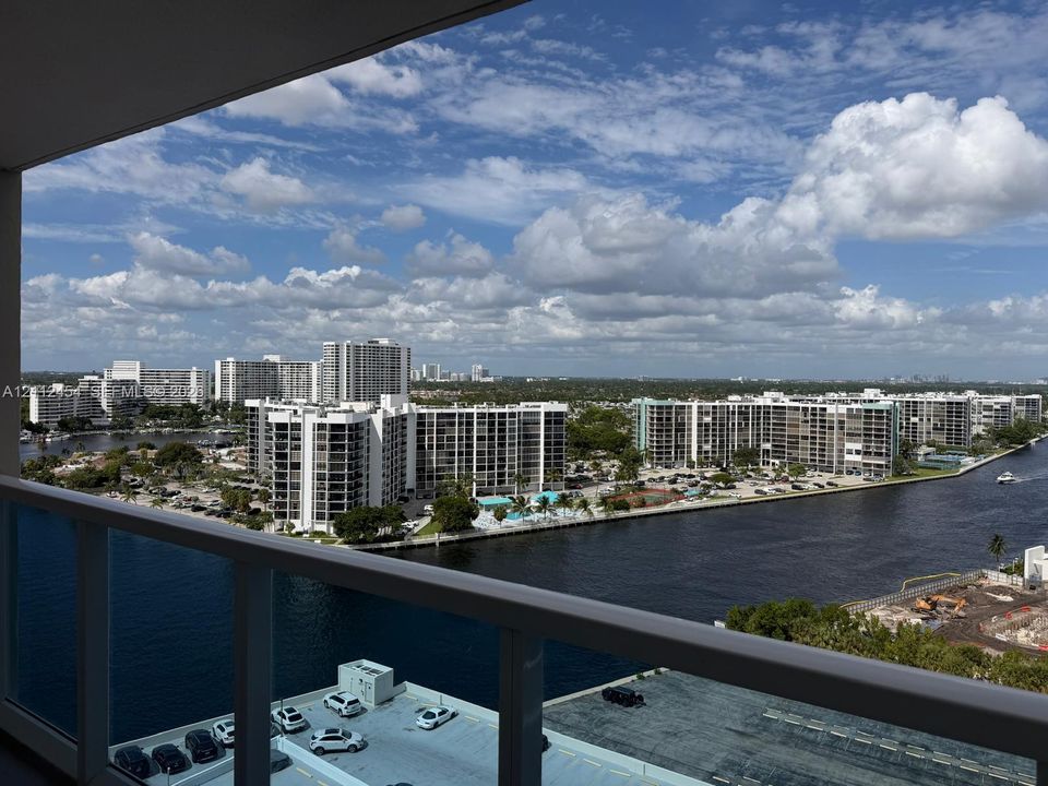 Covered balcony with a white metal railing overlooking a waterway and high-rise skyline