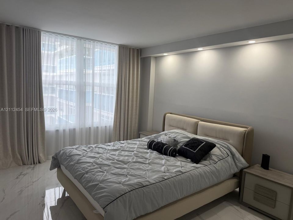 Floor-to-ceiling windows with layered drapery, stone-finish tile flooring, and integrated recessed ceiling lighting