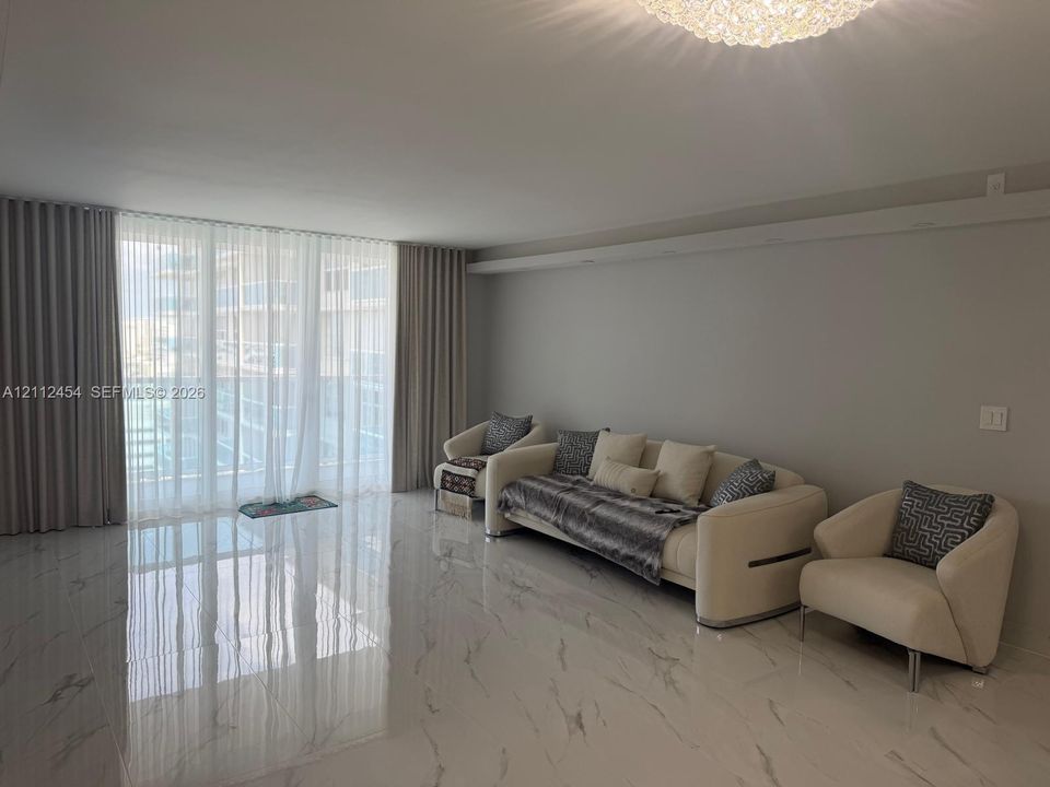 Polished stone-finish flooring, floor-to-ceiling drapery, and a recessed ceiling feature with a central tiered light fixture