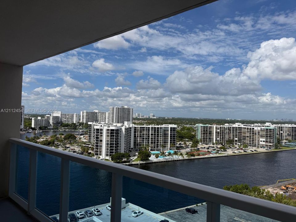 Private balcony featuring a white aluminum railing, oriented toward a waterway and urban skyline