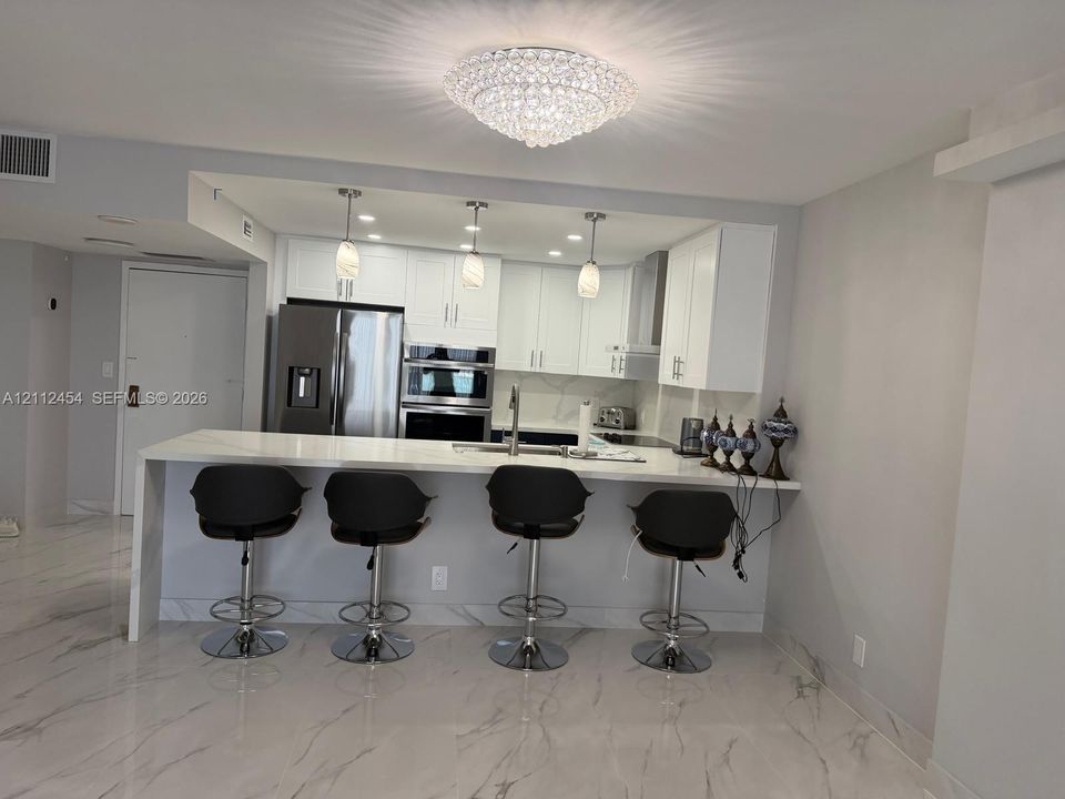 Kitchen featuring white cabinetry, a waterfall-edge stone countertop, stainless steel built-in double wall oven, pendant lighting, and stone-finish flooring