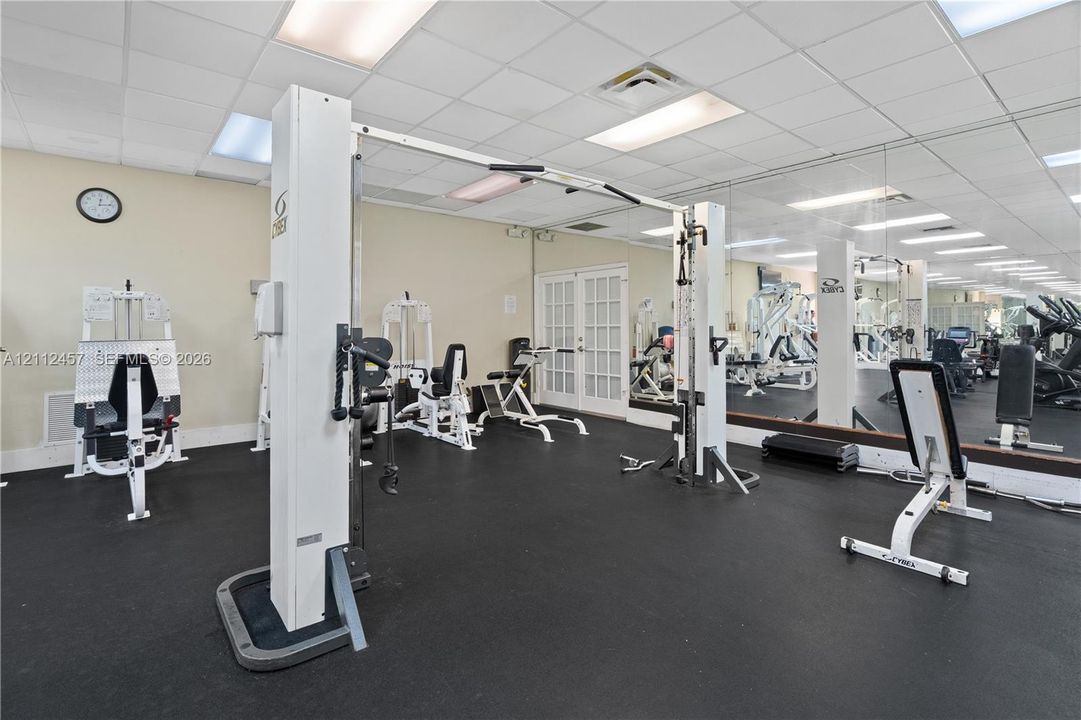 Fitness room featuring wall-to-wall mirrors, suspended ceiling grid, and durable rubber flooring