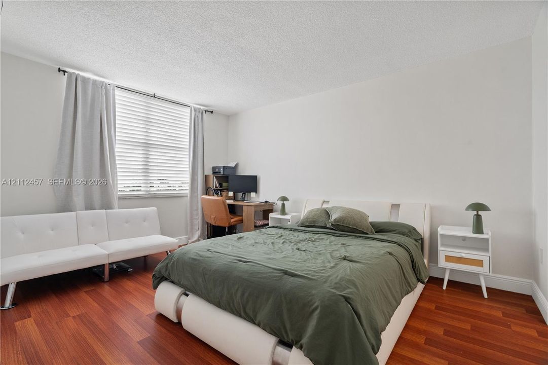 Bedroom featuring wood-finish flooring and a large window with horizontal blinds