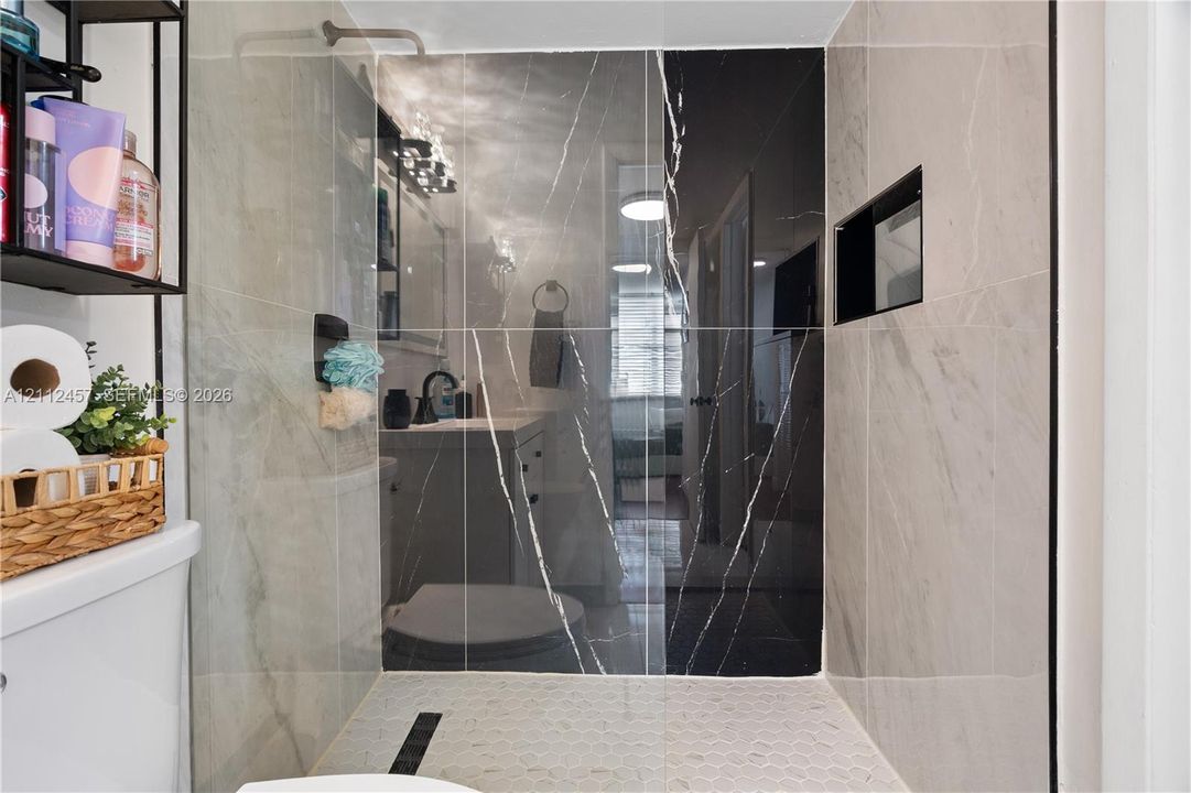 Walk-in shower featuring large-format light and dark veined tile, integrated wall niche, and hexagonal floor tile