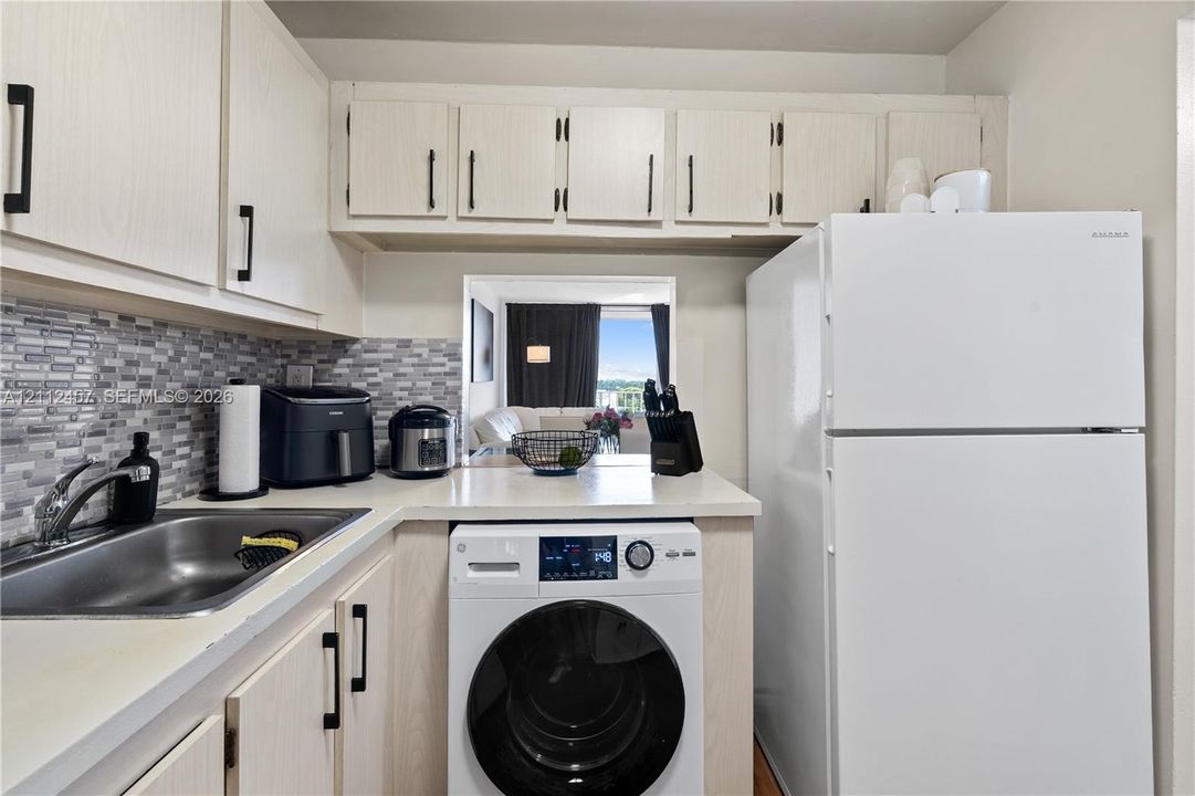 Kitchen featuring light-finish cabinetry with matte black hardware, mosaic tile backsplash, stainless steel sink with high-arc faucet, and a built-in front-load laundry appliance