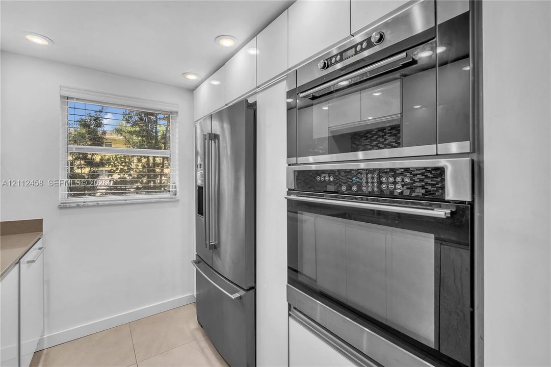 Kitchen featuring high-gloss white cabinetry, integrated stainless steel appliances, a built-in wall oven and microwave unit, recessed ceiling lighting, and large-format tile flooring