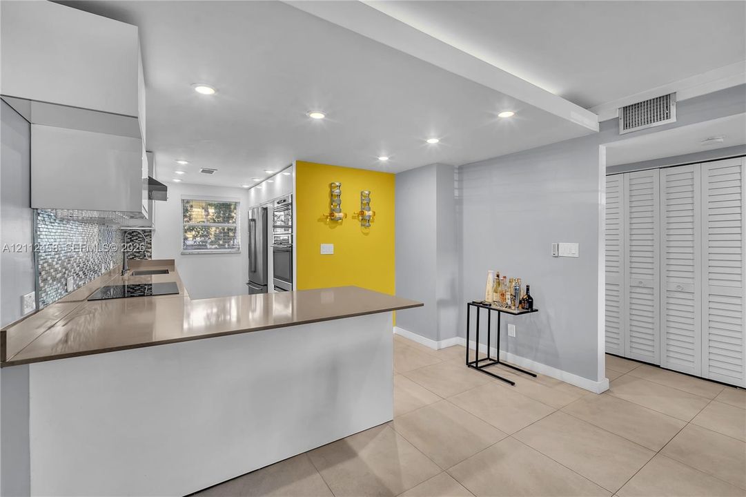 Kitchen featuring a solid-surface peninsula, stainless steel wall oven, flat-panel cabinetry, mosaic tile backsplash, and large-format neutral floor tile