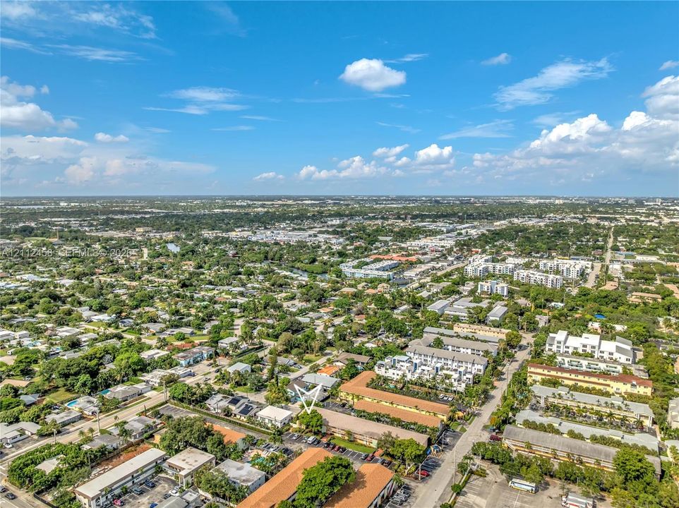 Aerial perspective of a multi-unit residential complex featuring low-rise buildings, terracotta-toned roofing, paved parking areas, and mature landscape trees