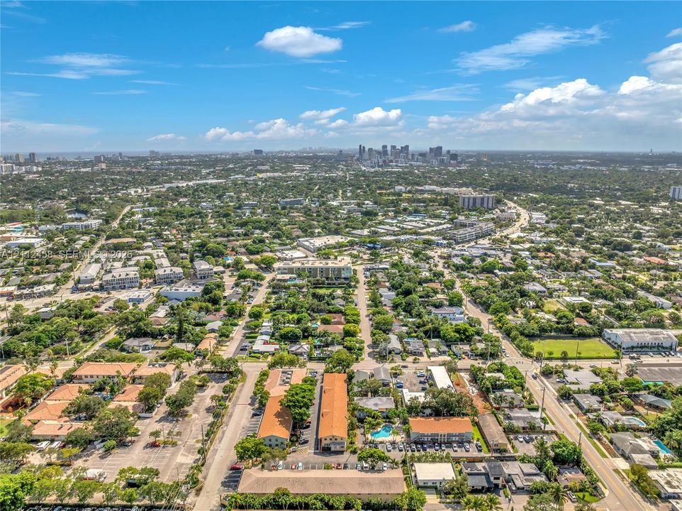 Aerial perspective of the residential grounds featuring low-rise multi-family structures, surface parking, a centrally located swimming pool, and established greenery