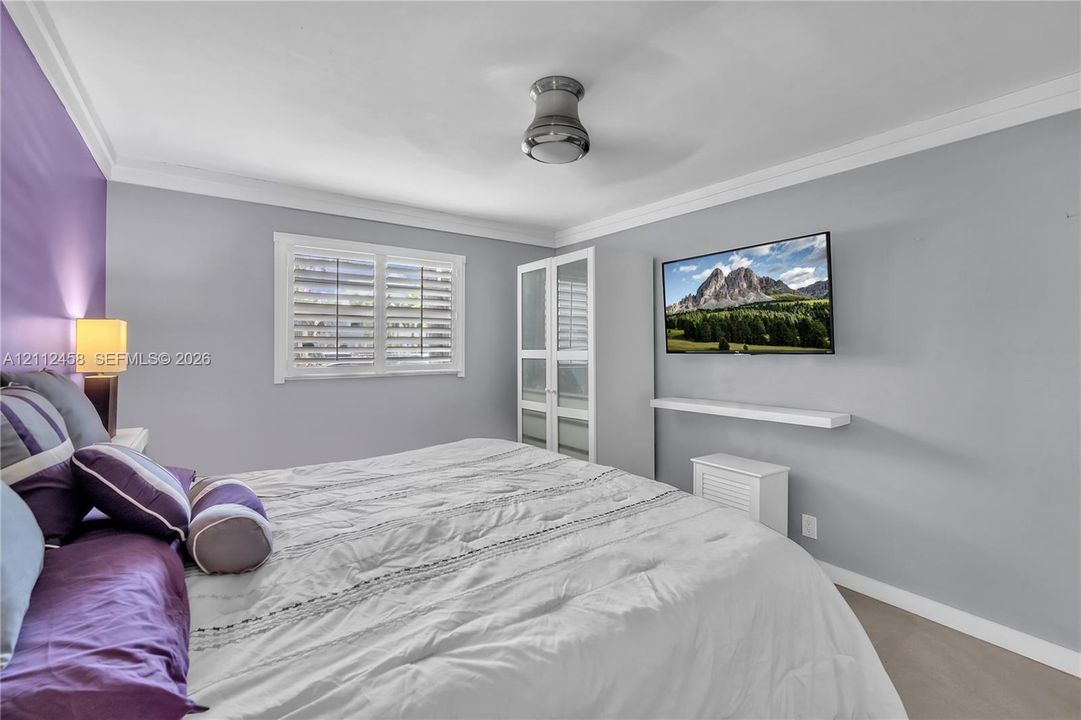 Interior space featuring crown molding, plantation shutters, a floor-to-ceiling built-in wardrobe with glass-paneled doors, and a wall-mounted floating shelf