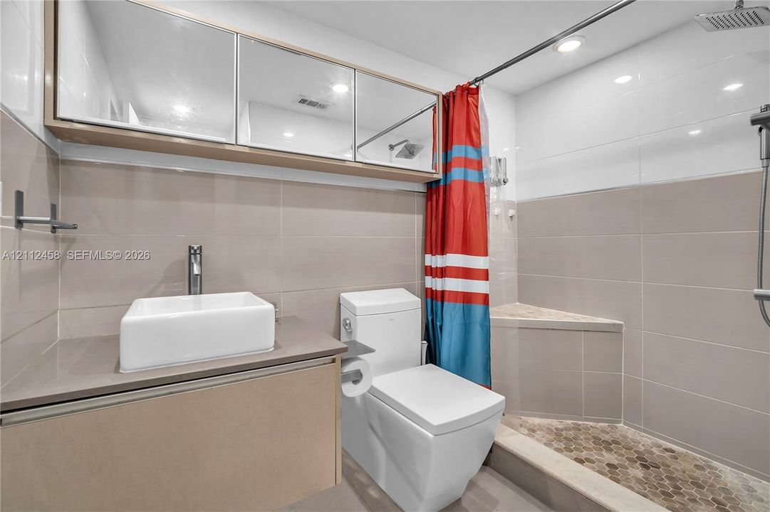 Bathroom featuring a floating vanity with a rectangular vessel sink, wall-mounted mirrored cabinetry, a walk-in shower with a built-in bench, and stone-finish wall tiling