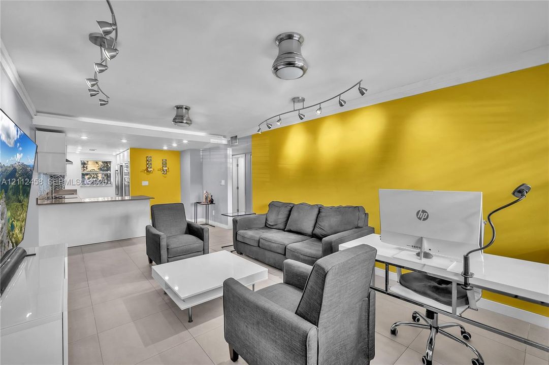 Open-concept living space featuring large-format tile flooring, multi-directional track lighting, and a kitchen peninsula with a stone-finish countertop