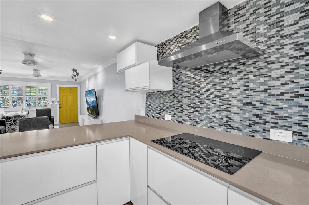 Kitchen featuring flat-panel white cabinetry, solid surface countertops, a glass mosaic tile backsplash, a stainless steel range hood, and a flush-mount electric cooktop