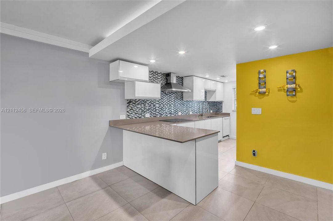 Kitchen featuring flat-panel white cabinetry, solid-surface countertops, a stainless steel range hood, a decorative tile backsplash, and ceramic tile flooring