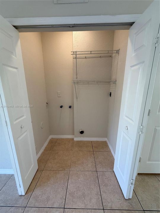 Utility closet featuring dual-folding doors, tile flooring, and integrated metal shelving