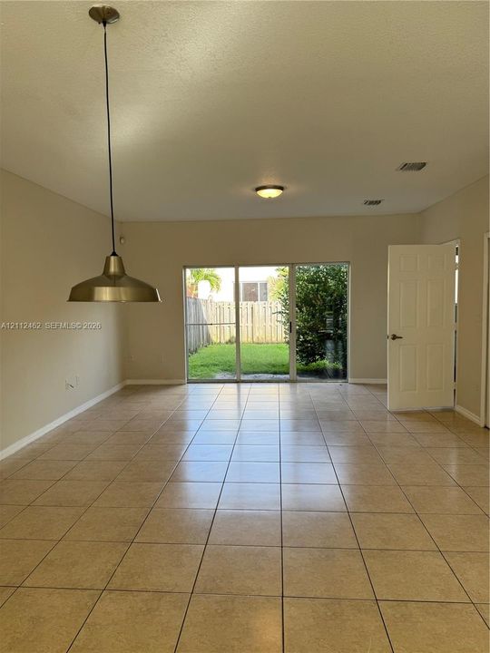 Tiled flooring throughout, sliding glass doors, metallic pendant lighting, flush-mount ceiling fixture, and exterior fencing