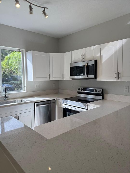 Kitchen featuring white shaker-style cabinetry, quartz countertops, stainless steel appliances, and a single-basin undermount sink