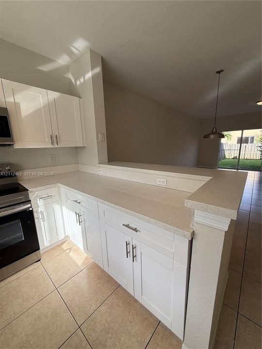 Kitchen featuring white shaker-style cabinetry, neutral stone-composite countertops, stainless steel appliances, ceramic tile flooring, and a breakfast bar