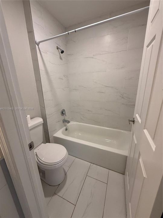 Full bathroom featuring large-format light-toned tile flooring, a tub-shower combination, and wall-to-wall light-toned tile surround