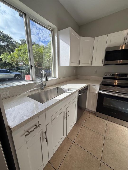 Kitchen featuring white shaker-style cabinetry, stainless steel appliances, quartz countertops, an undermount sink with a gooseneck faucet, and tile flooring