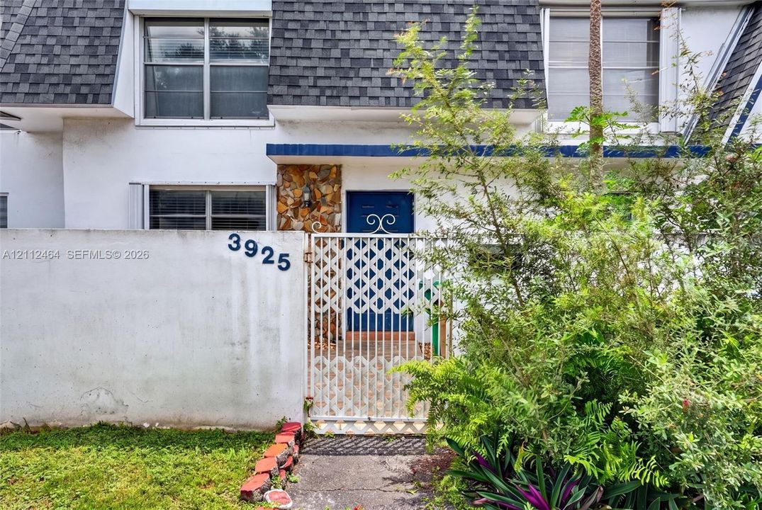 Exterior facade featuring a mansard roof, white stucco wall, stone veneer accent, and a decorative metal gate entry