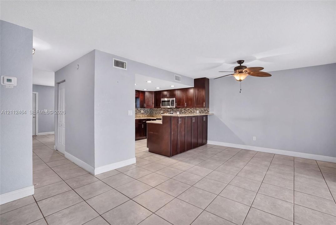Kitchen featuring dark-toned wood cabinetry, stone-style tile backsplash, stainless steel microwave, and peninsula counter, finished with ceramic tile flooring