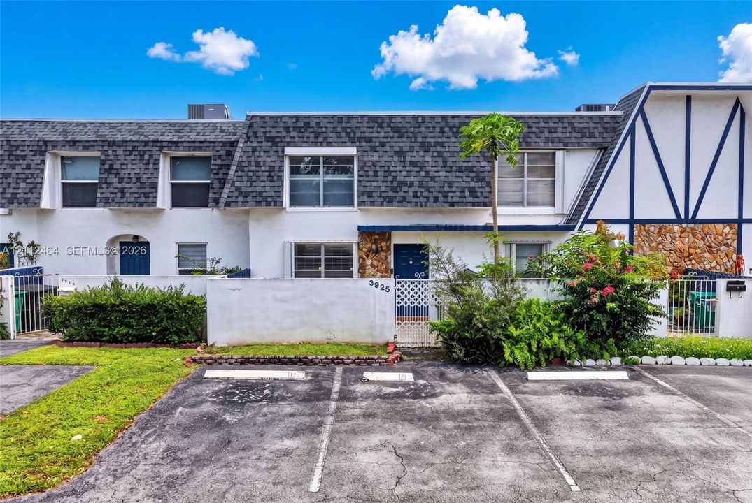 Multi-story exterior featuring a mansard roof, stucco siding, stone veneer accents, and private gated courtyard entrances with dedicated parking spaces