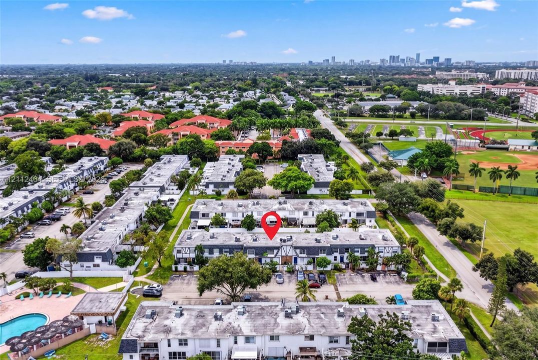 Aerial perspective of a multi-unit property complex featuring concrete block construction, flat roof structures, paved parking areas, and mature trees