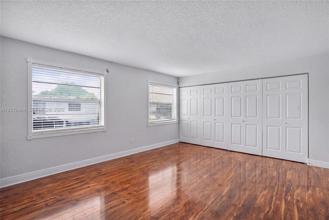 Wood-finish flooring, two large windows with horizontal blinds, and a set of multi-panel bi-fold closet doors