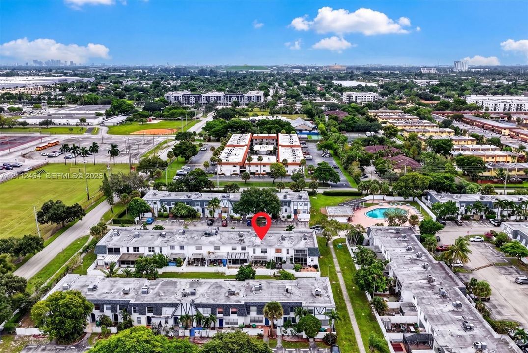 Aerial perspective of the residential complex featuring multi-story townhome structures, expansive green space, and a community swimming pool