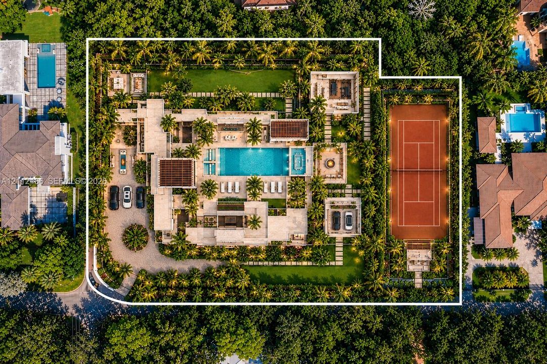 Aerial perspective of a sprawling estate featuring a clay tennis court, large swimming pool with built-in spa, expansive manicured grounds, covered patios, and a circular driveway