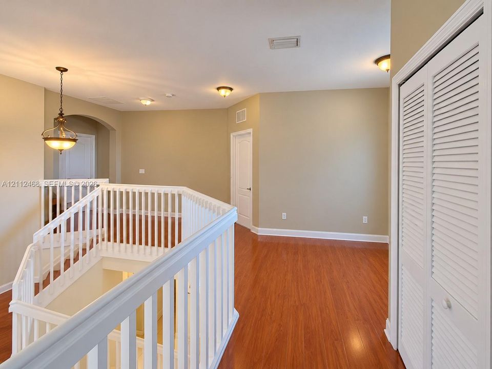 Wood-finish flooring, white spindle staircase railing, louvered bi-fold closet doors, arched architectural opening, and hanging pendant lighting