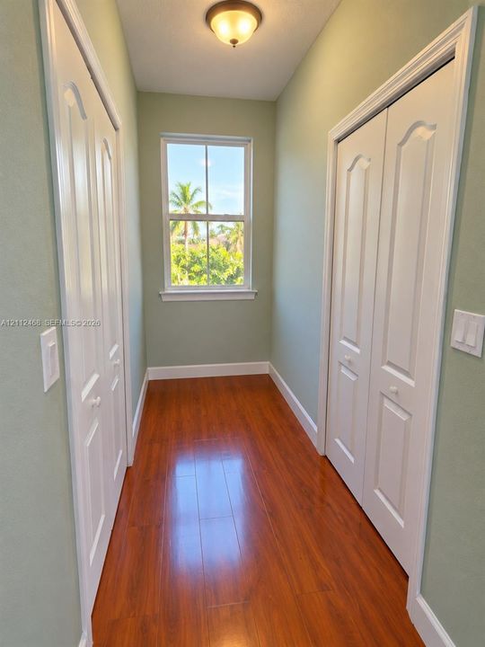 Wood-finish flooring, dual bifold closets with arched panel doors, and a double-hung window with exterior greenery