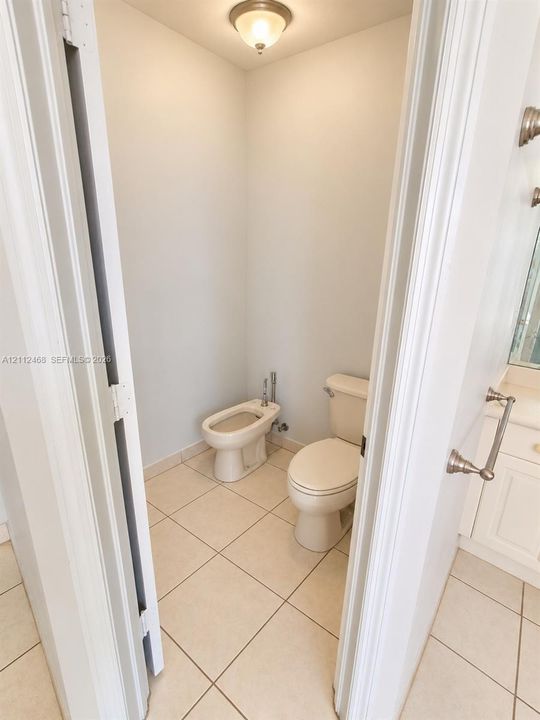 Water closet featuring a two-piece toilet, bidet, neutral tile flooring, and a flush-mount ceiling light fixture