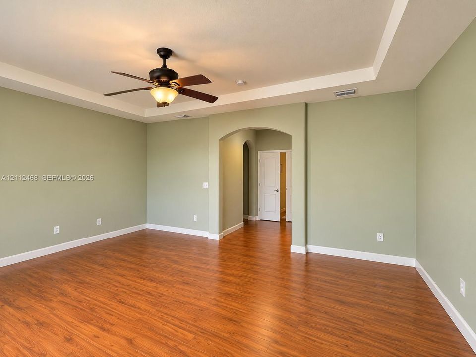 Room featuring wood-finish flooring, a tray ceiling, an arched entryway, and an attached ceiling fan with a light fixture