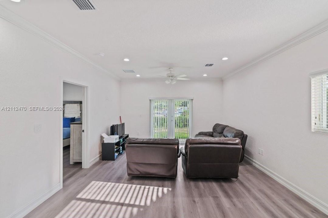 Living area featuring wood-finish flooring, recessed lighting, crown molding, a ceiling fan, and sliding glass doors with vertical blinds