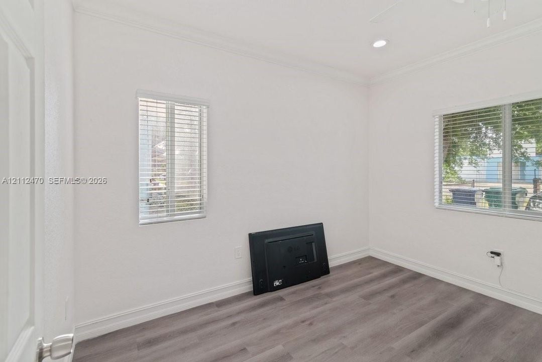 Neutral interior room featuring wood-finish flooring, crown molding, recessed lighting, and dual windows with horizontal blinds