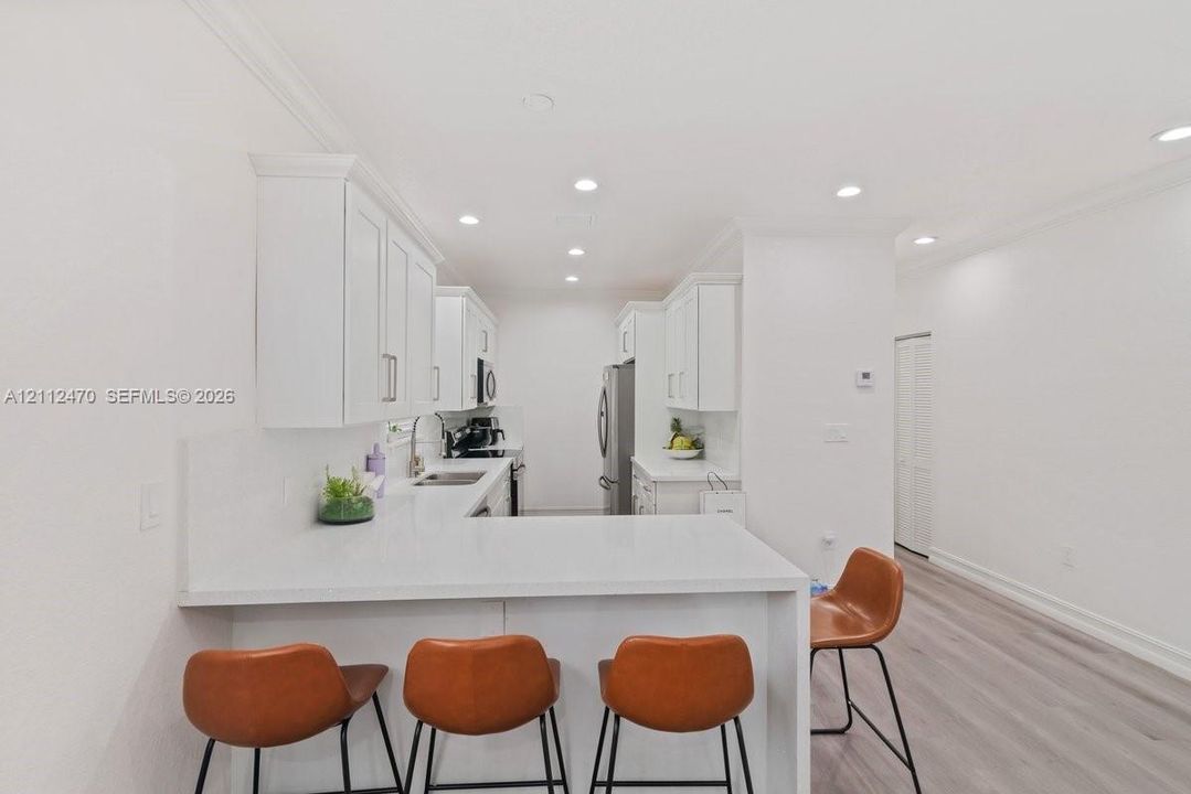 Kitchen featuring white cabinetry, solid-surface countertops, recessed ceiling lighting, and wood-finish flooring