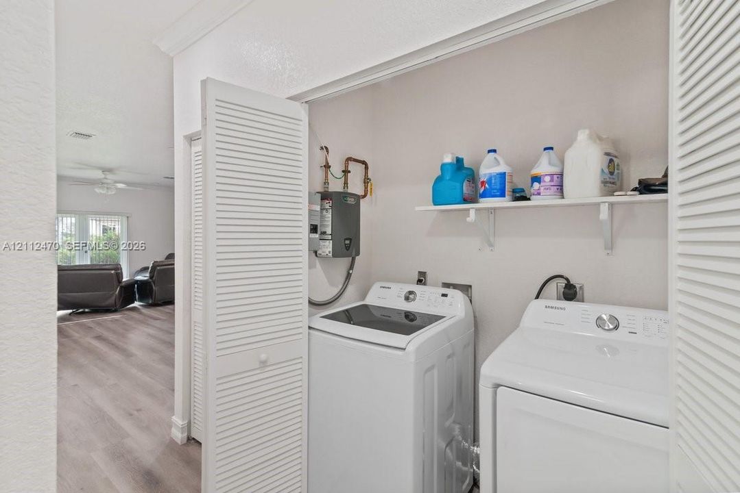 Laundry area featuring louvered bi-fold doors, wood-finish flooring, and a wall-mounted shelving unit
