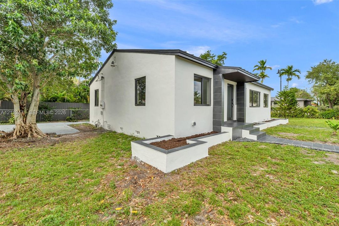 Single-story exterior featuring light-toned stucco siding, dark-toned masonry accents, a raised concrete entryway, a built-in garden planter, and a tiled walkway