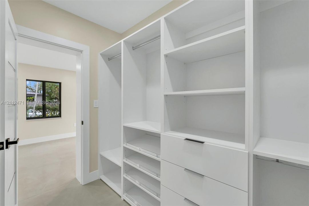 Custom walk-in closet featuring white built-in shelving, integrated garment rods, tiered drawer storage, and matte black hardware